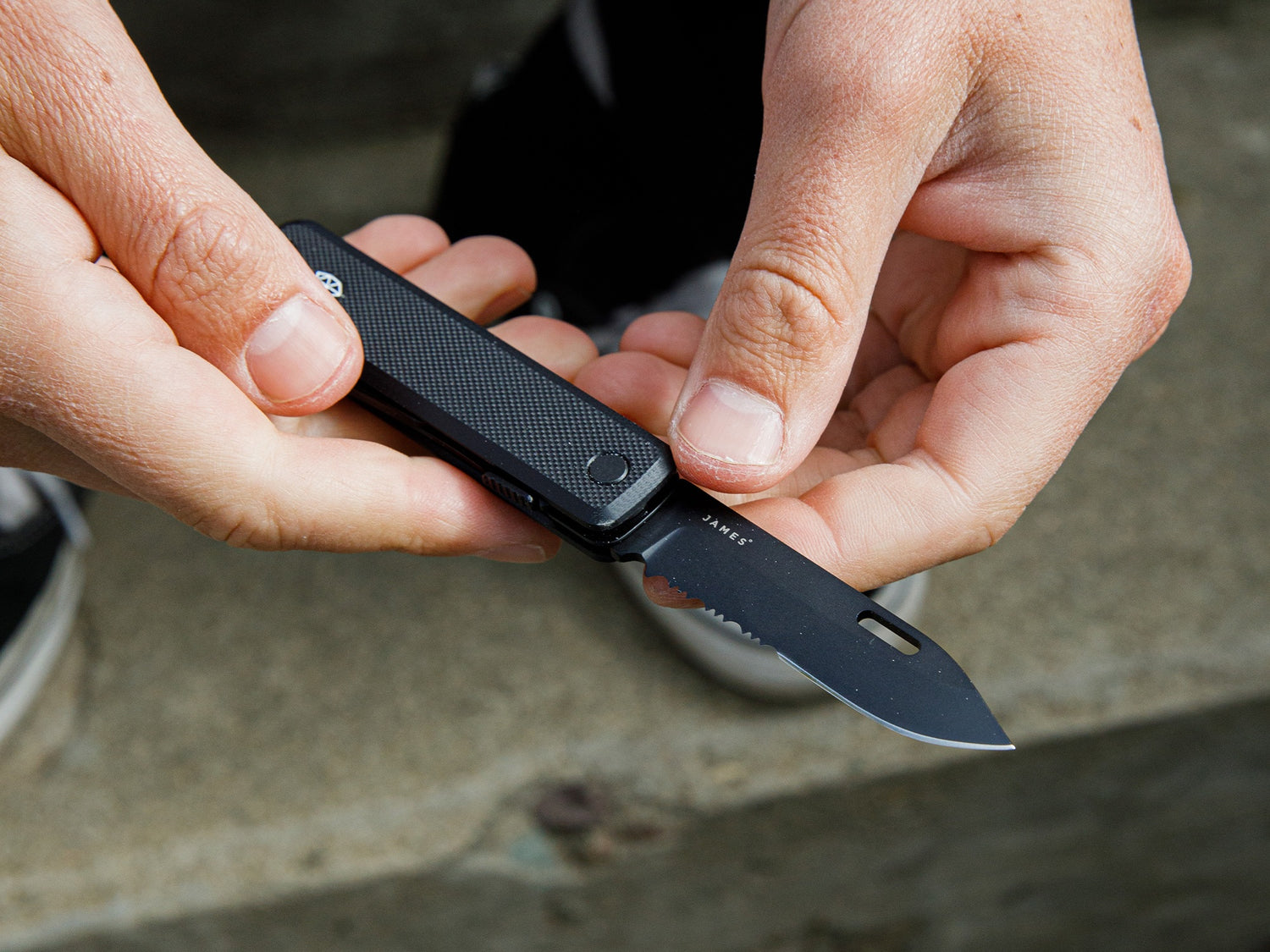 A man holding The Ellis EDC multitool pocket knife with the serrated blade open.