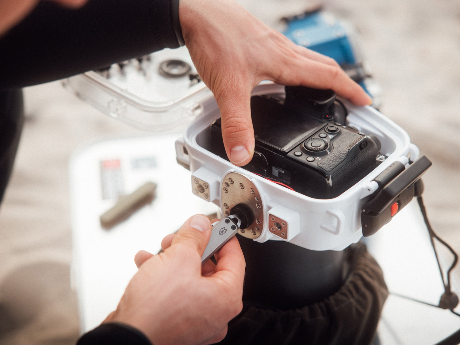 A man using his Elko keychain pocket knife to screw on the water housing of his camera.