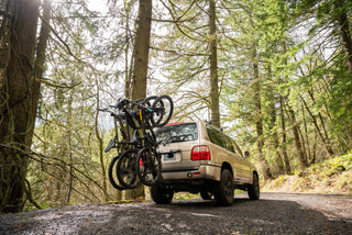 An SUV with mountain bikes on a tailgate rack in the forest.