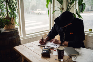 A man sketching in a notebook at a cafe with his Bolen twist pen.