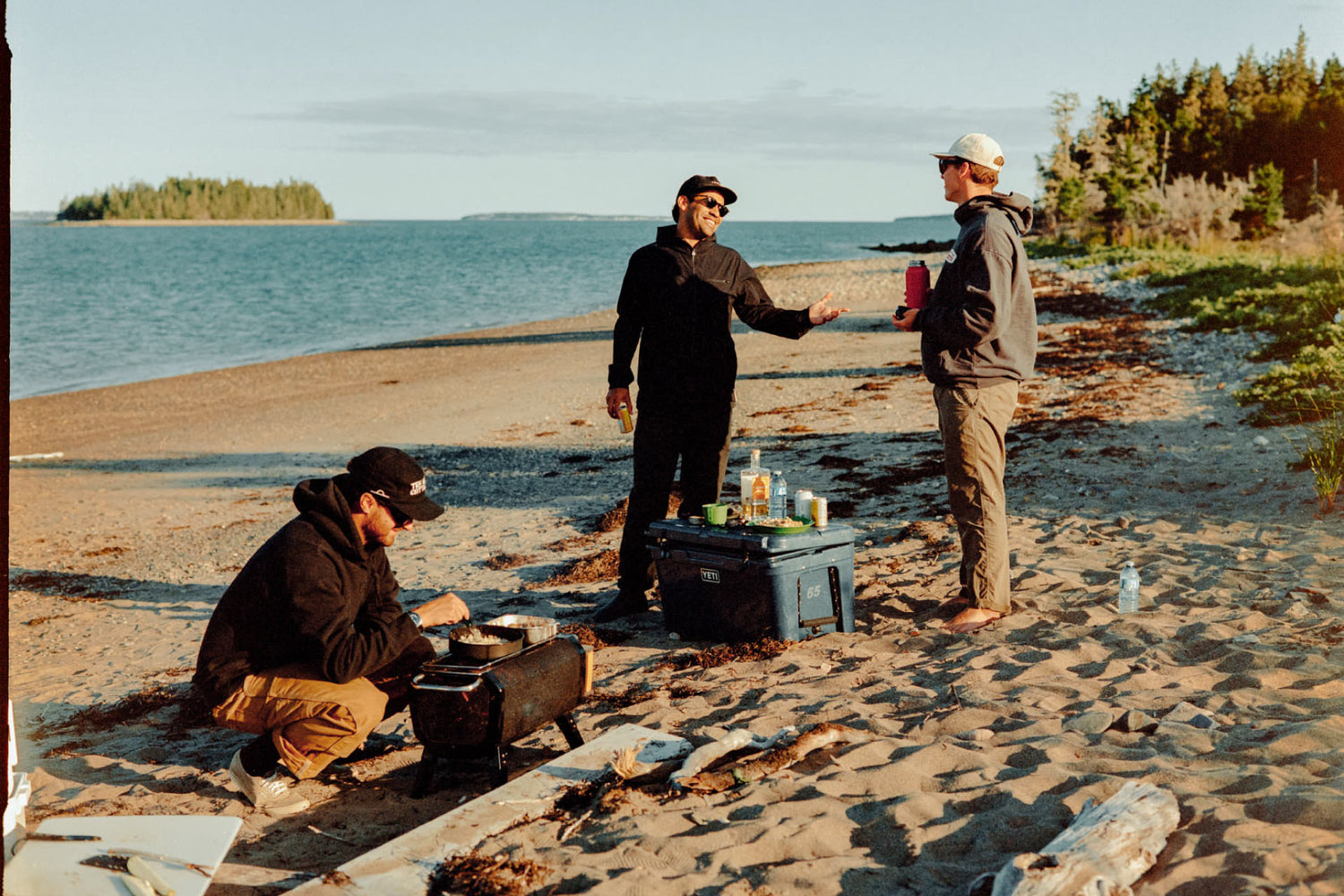 Three guys cooking food while handing out on a beach in Nova Scotia.