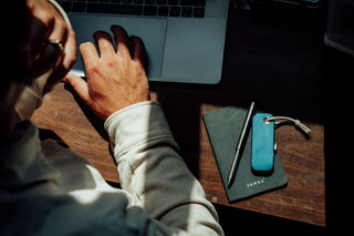 A surfboard shaper designing on a laptop with his pen, notebook, and EDC Palmer utility knife on the desk.