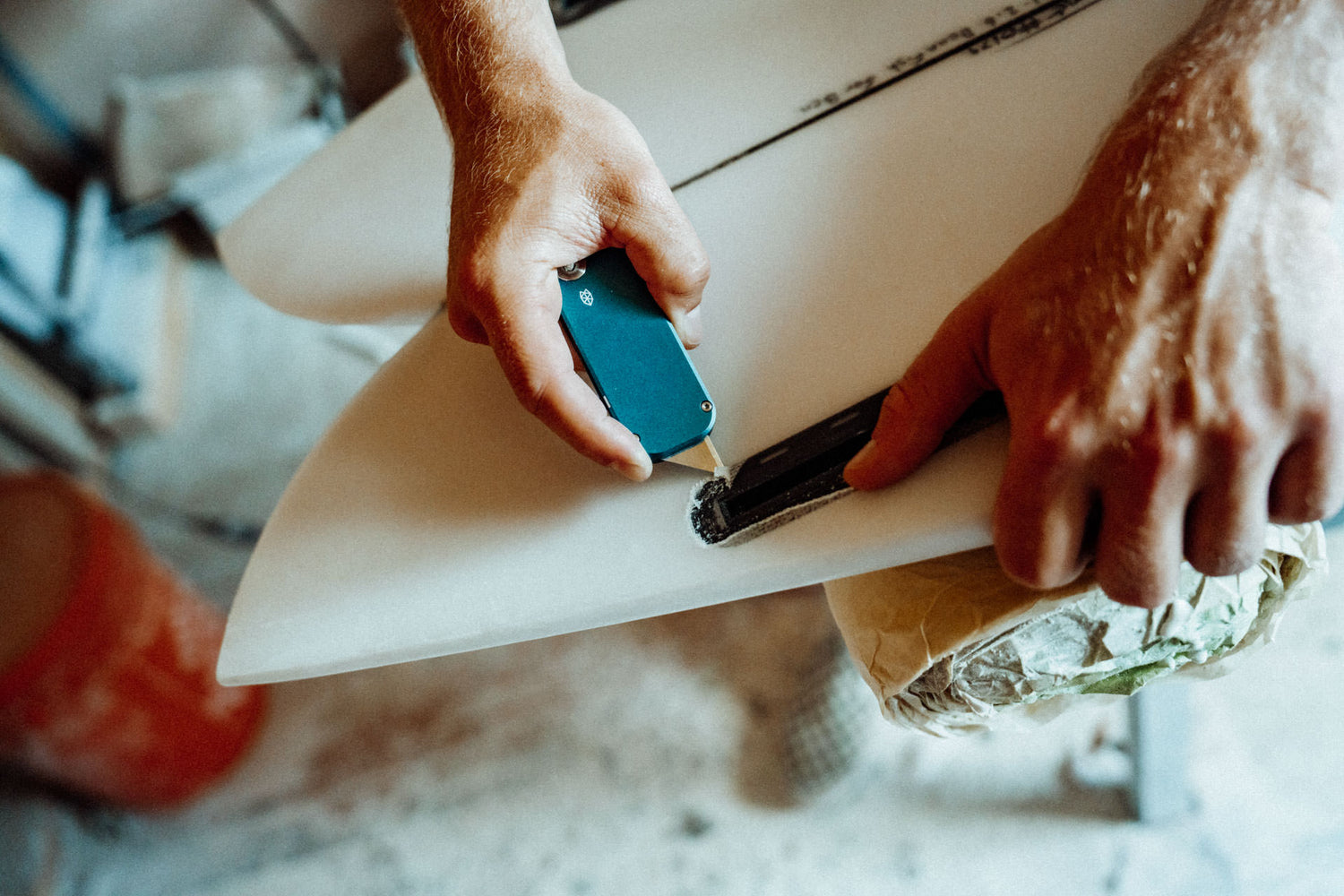 A surfboard shaper repairing a board using his Palmer EDC utility box cutter knife to cut away the damage area.