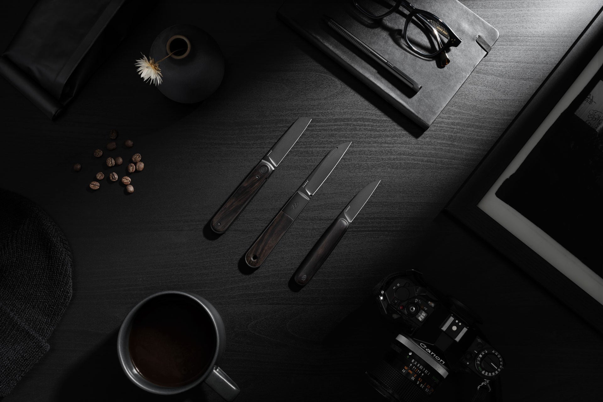 The Ebony collection of pocket knives on a desk top with everyday objects.