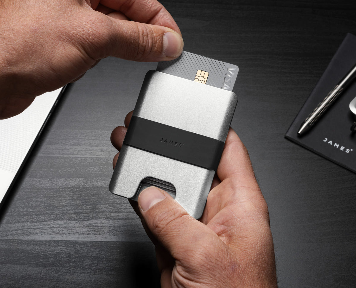 A man removing a credit card from The Lowe minimalist card holder wallet in silver and black.