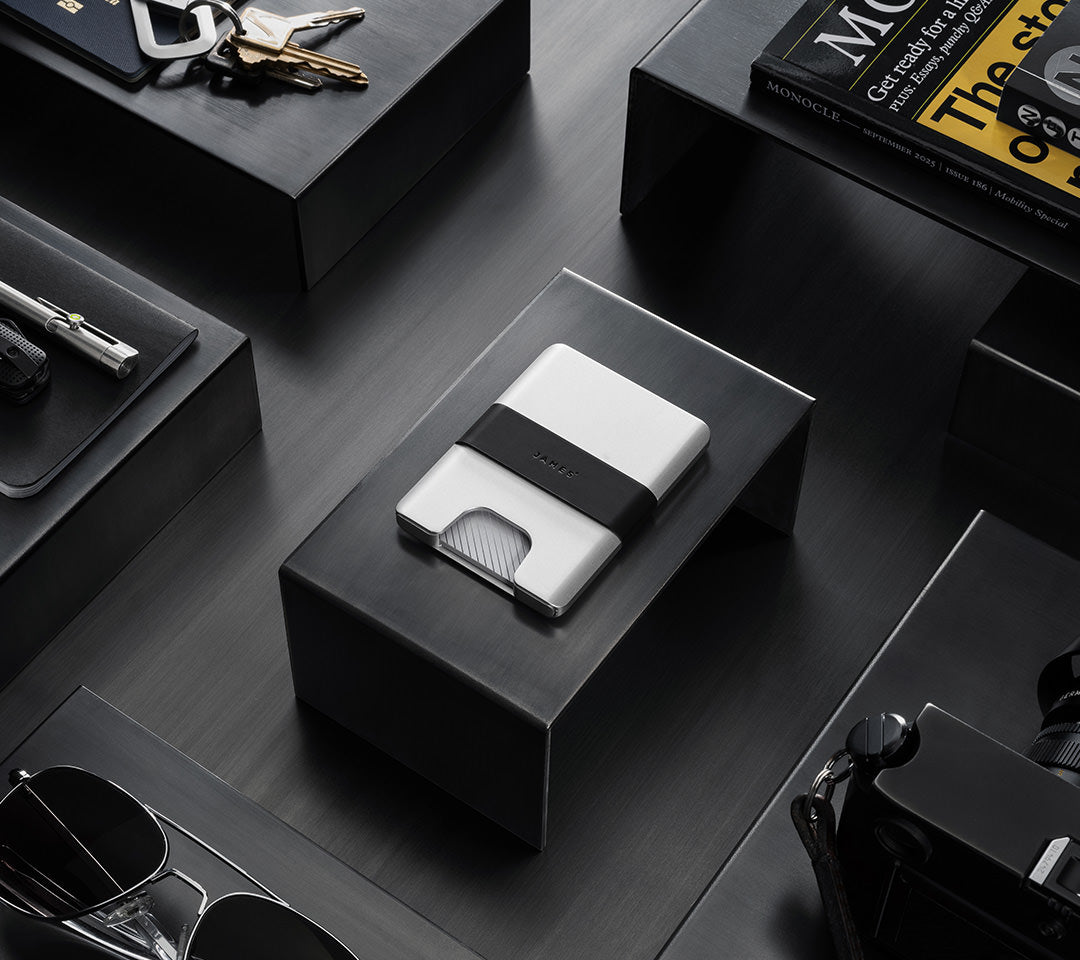 Silver wallet on a black box with keys and books in the background.