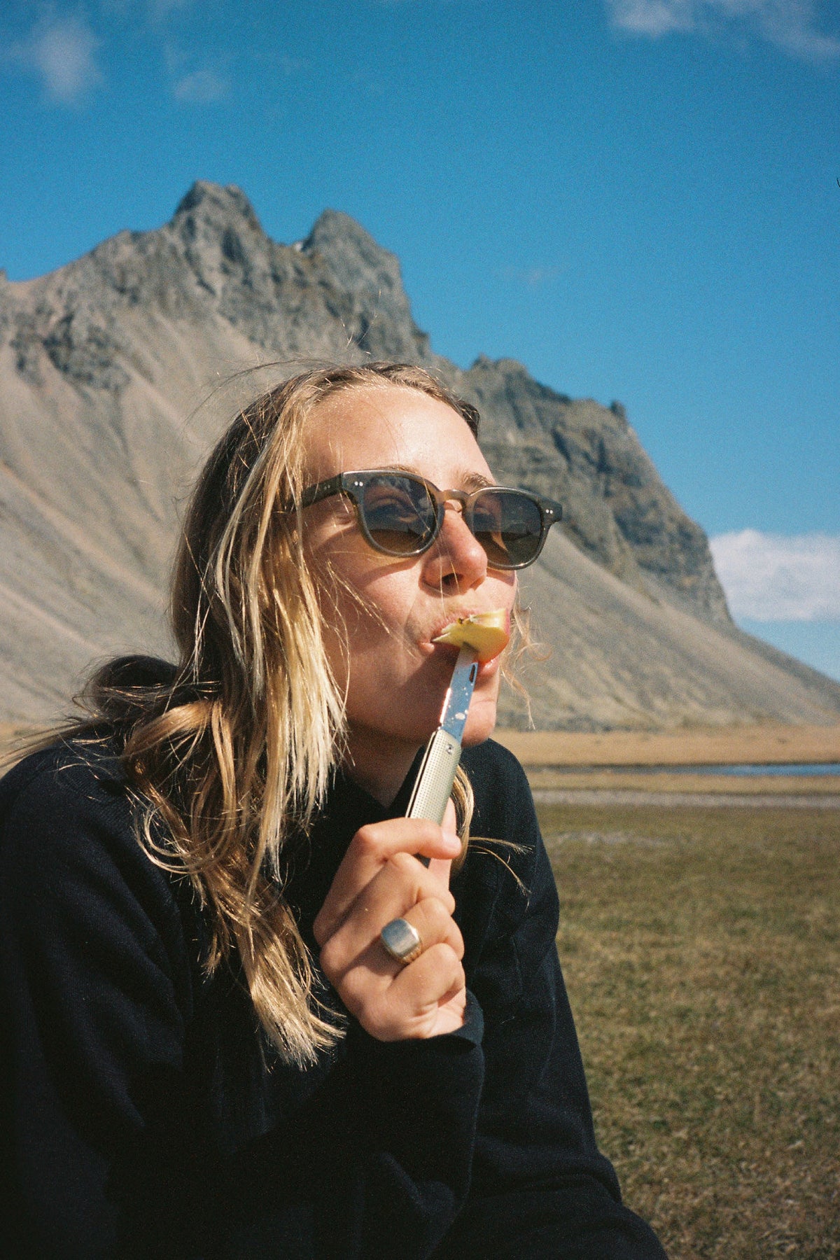 Snowboarder, surfer, and photographer Caley Vanular eating an apple with her Ellis slip joint pocket knife in grove.