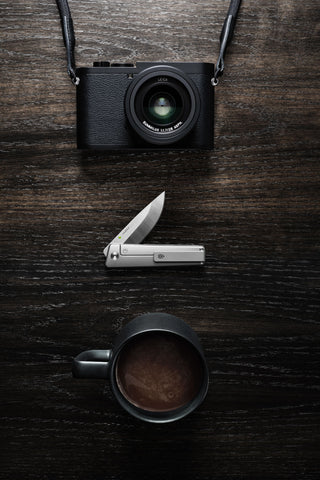 The Chapter 2 knife with a camera and cup of coffee.