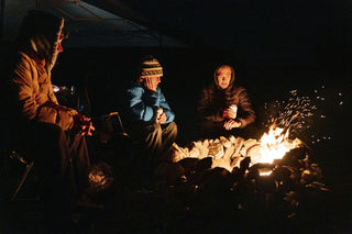 Three men having beers next to a fire in the desert.