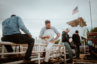 Josh Rosen sitting on a fence with cowboy hat in hand.